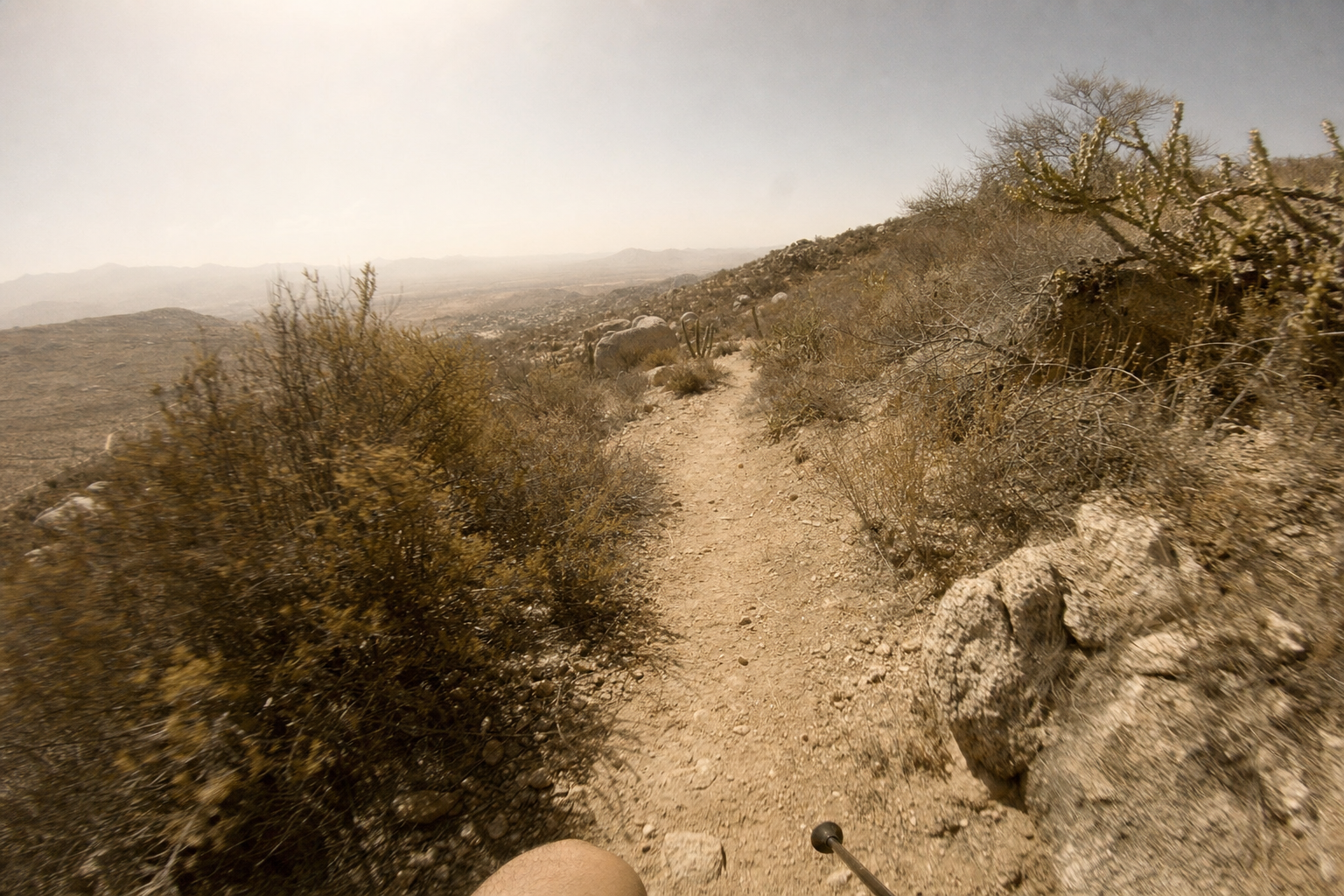 First-person view running down a dusty desert singletrack in the heat.
