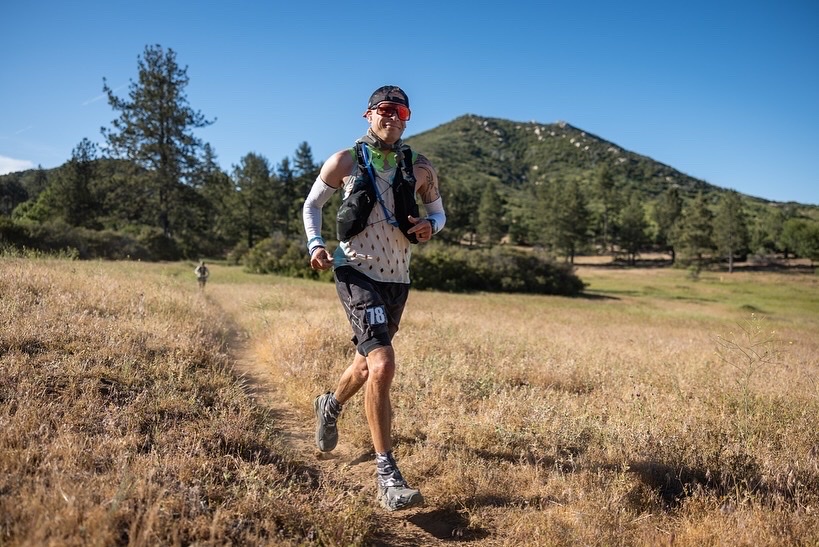 Ricky Roane running a dry single-track trail through golden grass during an ultramarathon.